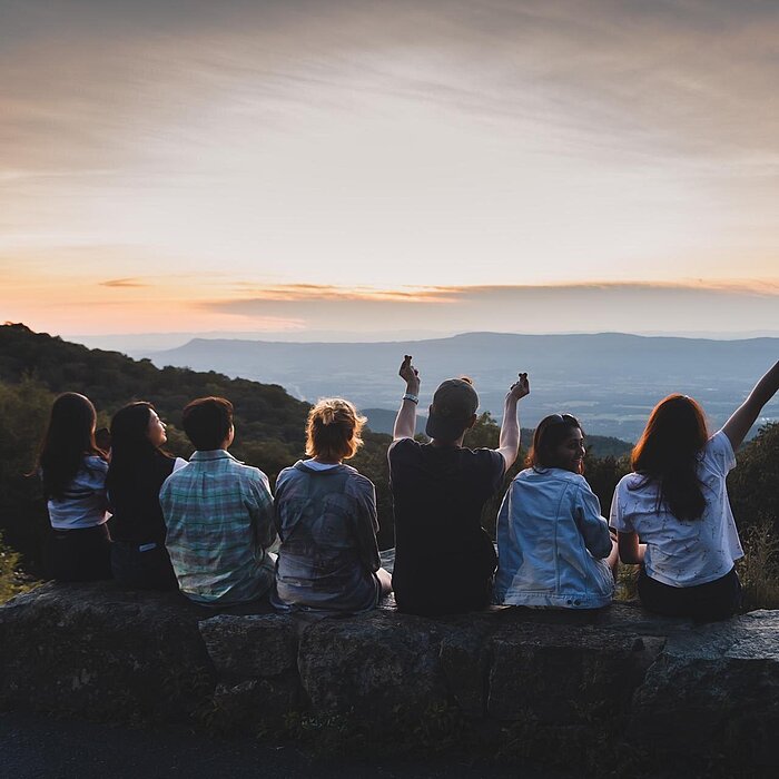 Rückenansicht von einer Gruppe, sitzend, auf einem Felsen, Sonnenuntergang